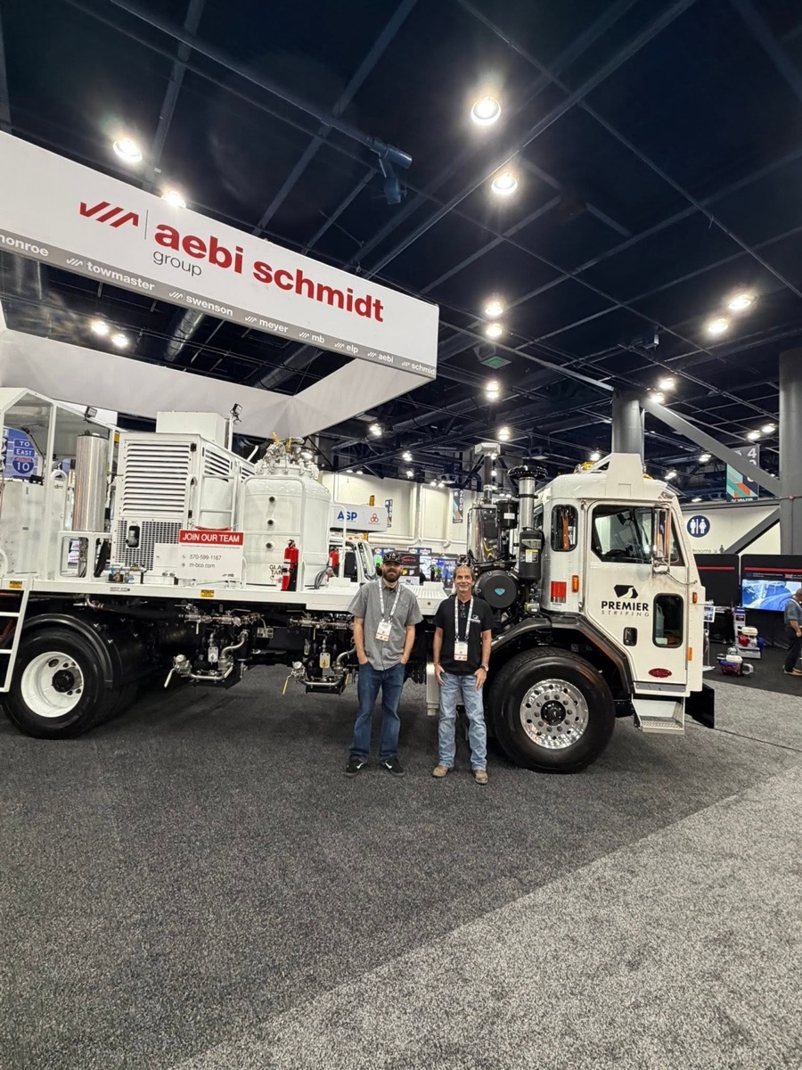 Two Premier Striping team members standing beside the line-striping truck